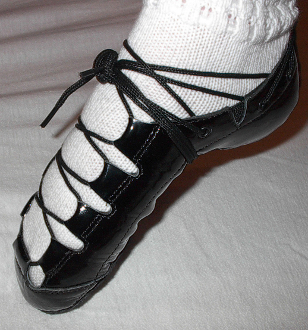 A pair of Celtic Choice Black Patent Leather shoes on a person's feet.