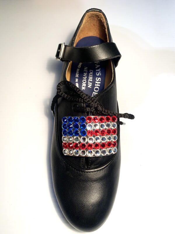 A black shoe with Flag of the United States Buckles on it.